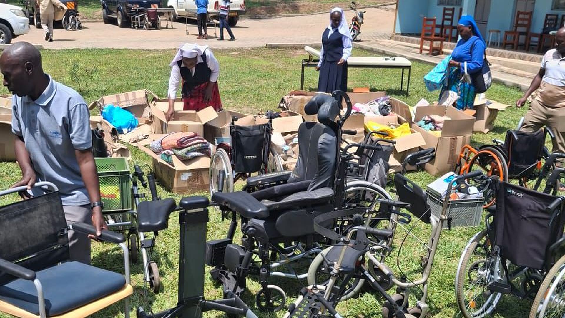 Ordensschwestern und Helfer packen in Uganda Kartons mit Hilfsgütern aus; davor stehen Rollstühle und Gehhilfen.