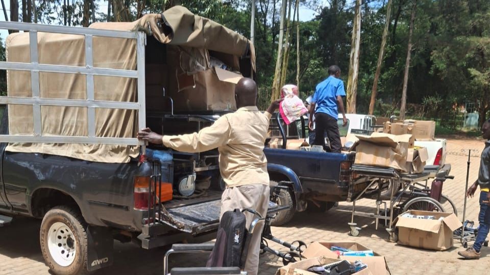Helfer in Uganda laden Rollstühle, Gehhilfen und Kartons von Pick-ups ab und sortieren sie.