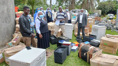 Helferinnen und Helfer in Uganda stehen zwischen ausgepackten Hilfsgütern, Kisten und Kartons.